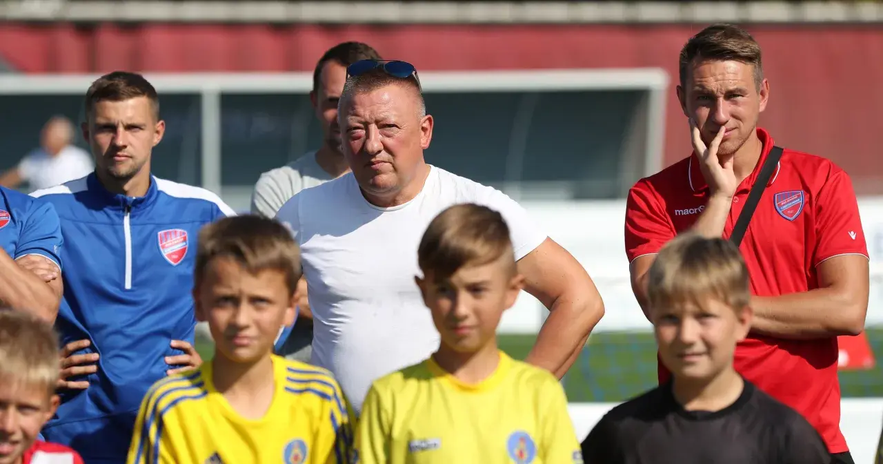 Marek Śledź, trener, w białej koszulce, stoi wśród młodych piłkarzy na boisku.