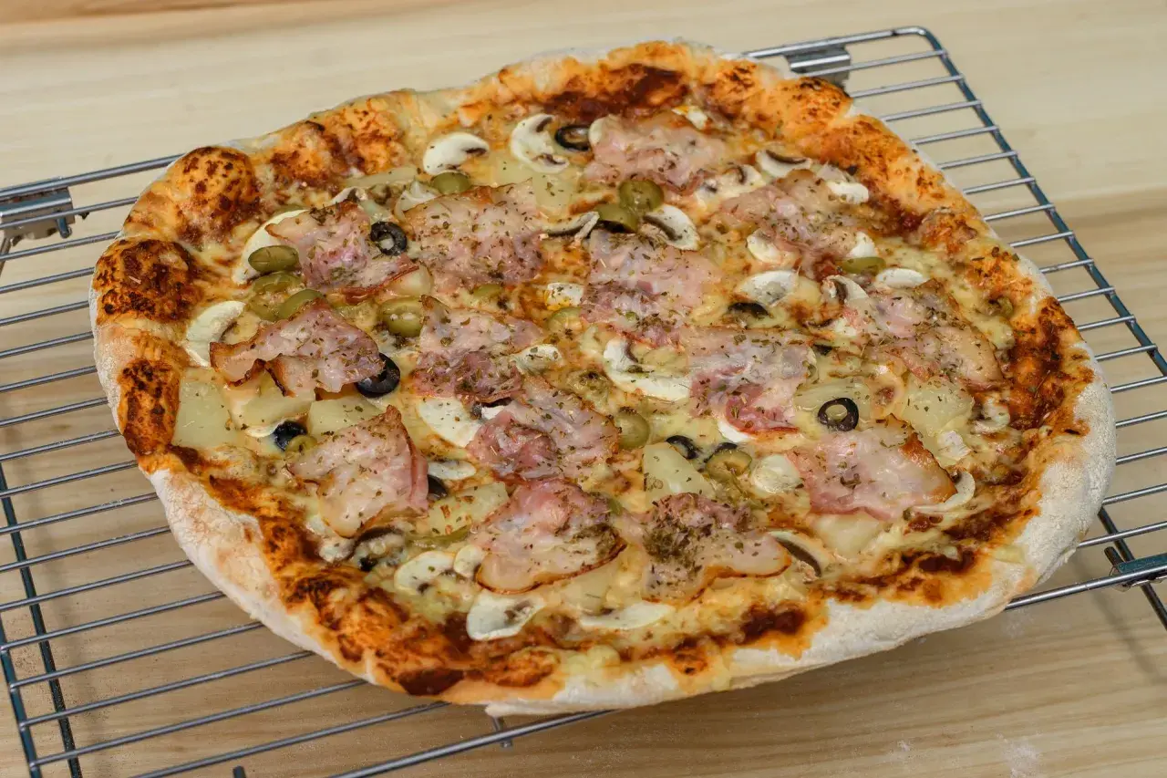 Pyszna pizza z szynką, pieczarkami, oliwkami i ananasem. Idealna na rodzinny obiad, zastanawiasz się ile piec pizze?
