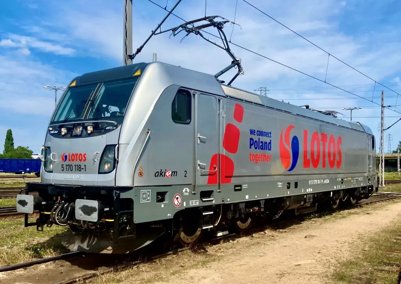 Srebrna lokomotywa Traxx z napisem LOTOS i hasłem "we connect Poland together" stoi na torach.