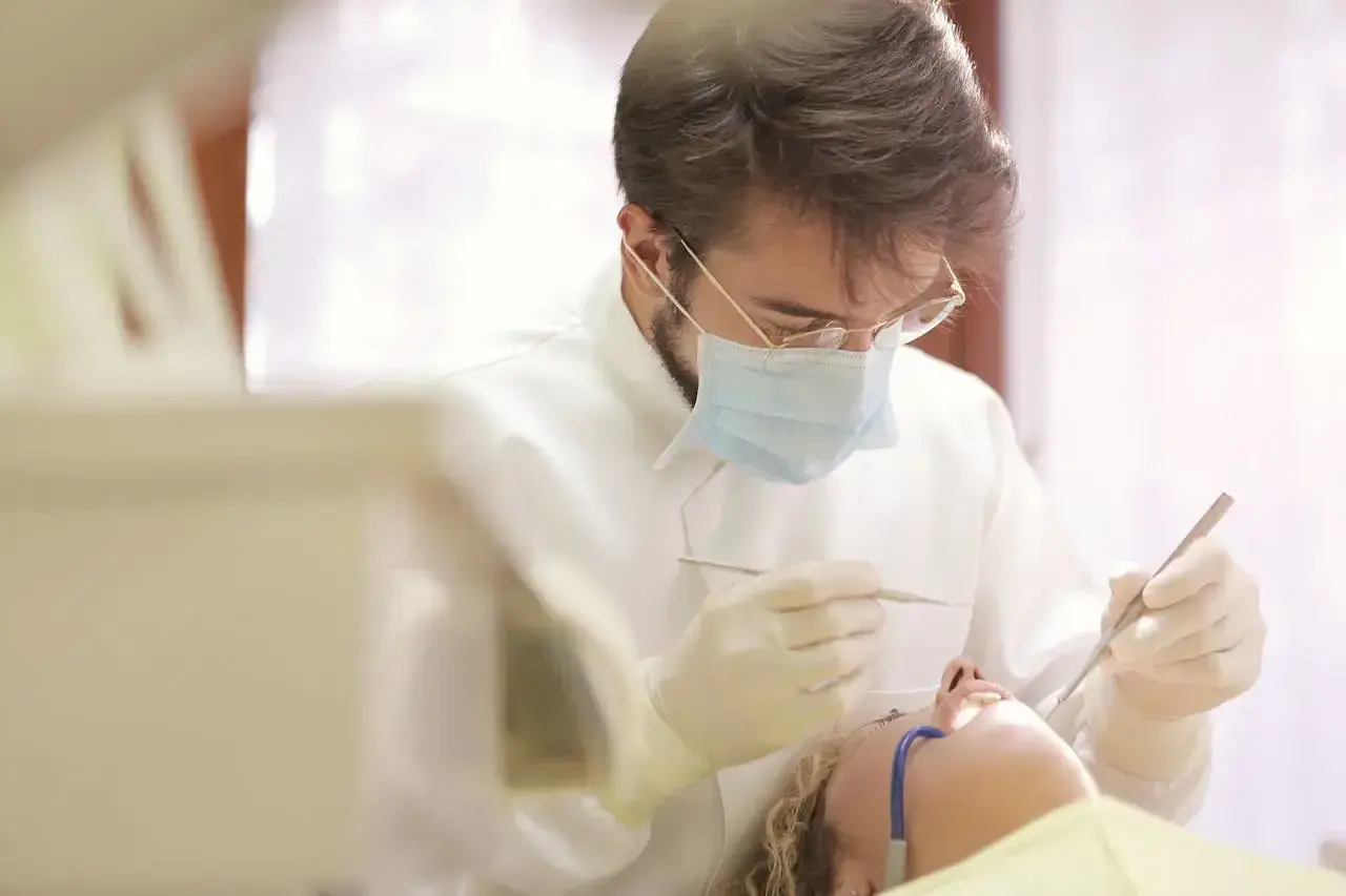 Dentysta w masce i rękawiczkach wykonuje zabieg. Pacjentka leży na fotelu. Pytanie o ile l4 po wyrwaniu ósemki.