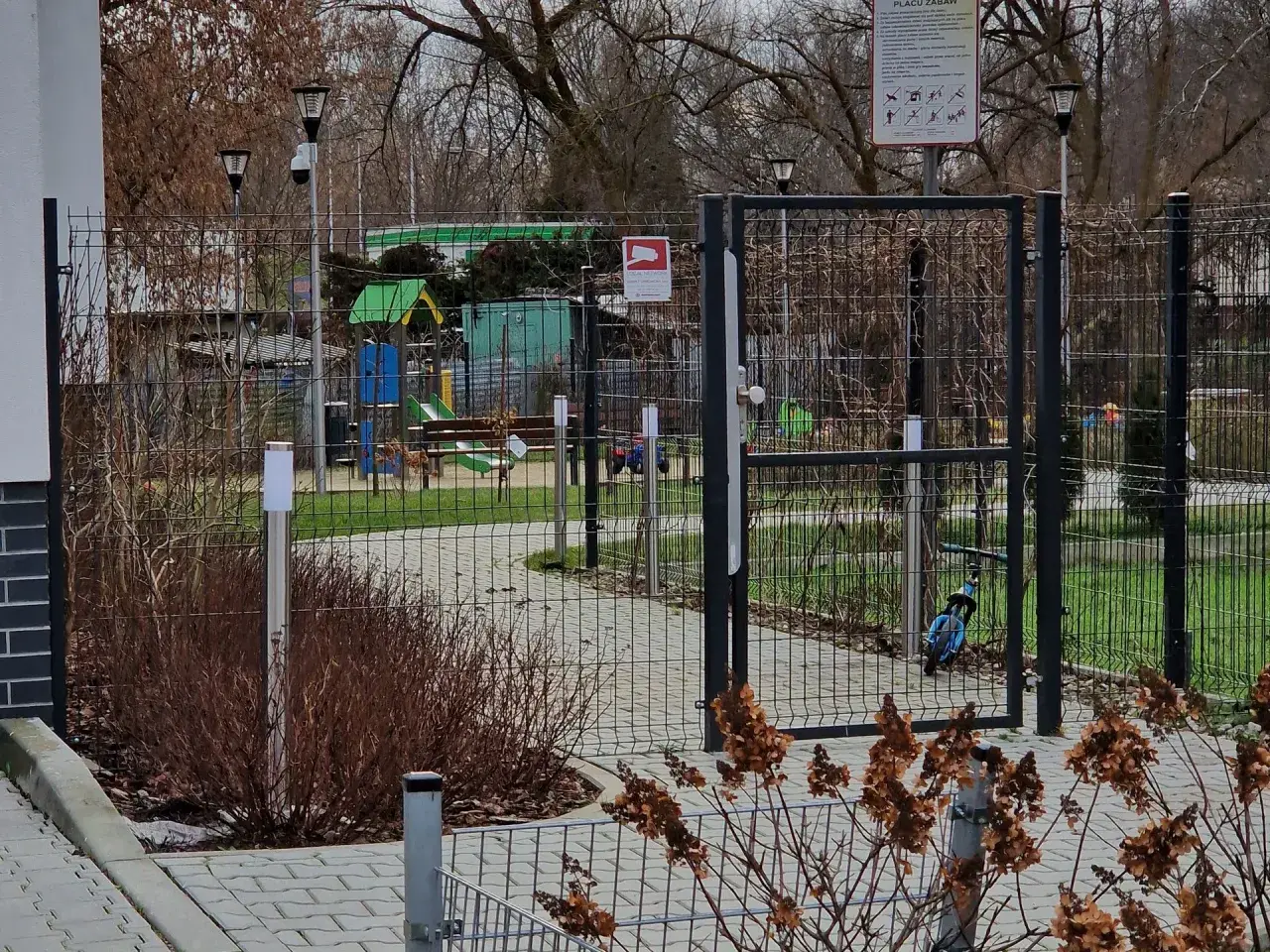 Prawda o ustawie która ma zakazać grodzenia osiedli w dużych miastach: ogrodzony plac zabaw z bramą i tablicą informacyjną.