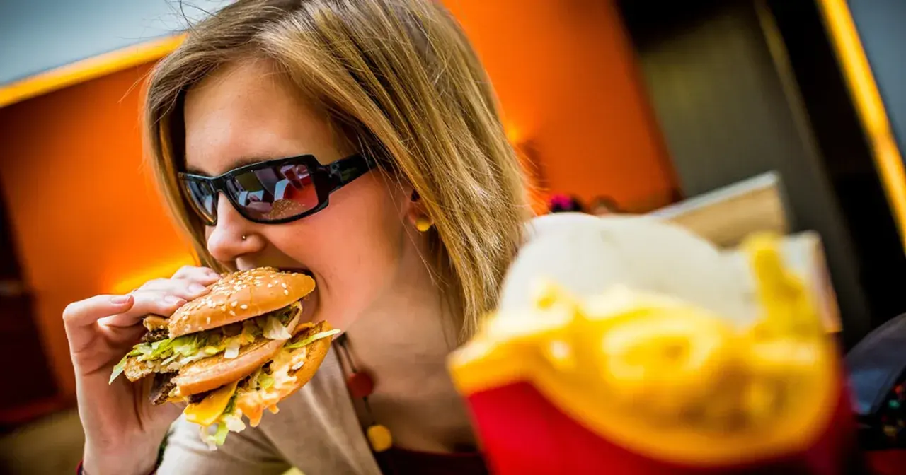 Dziewczyna w okularach je pysznego mcmuffin wieprzowy z jajkiem. Obok frytki.