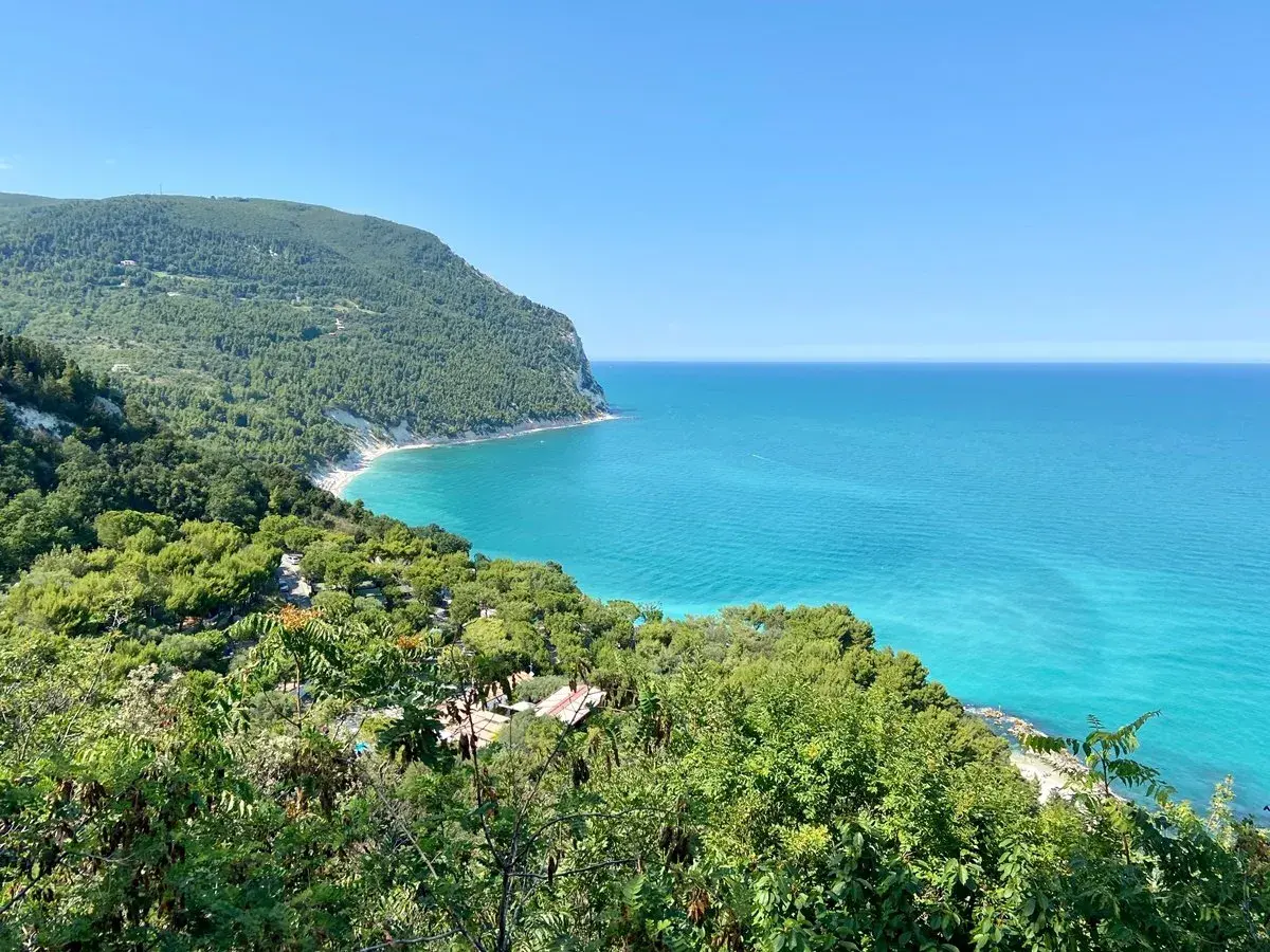 Vista mozzafiato sulla costa marchigiana, un gioiello tra le 10 cose da vedere nelle Marche. Mare turchese e verde lussureggiante.
