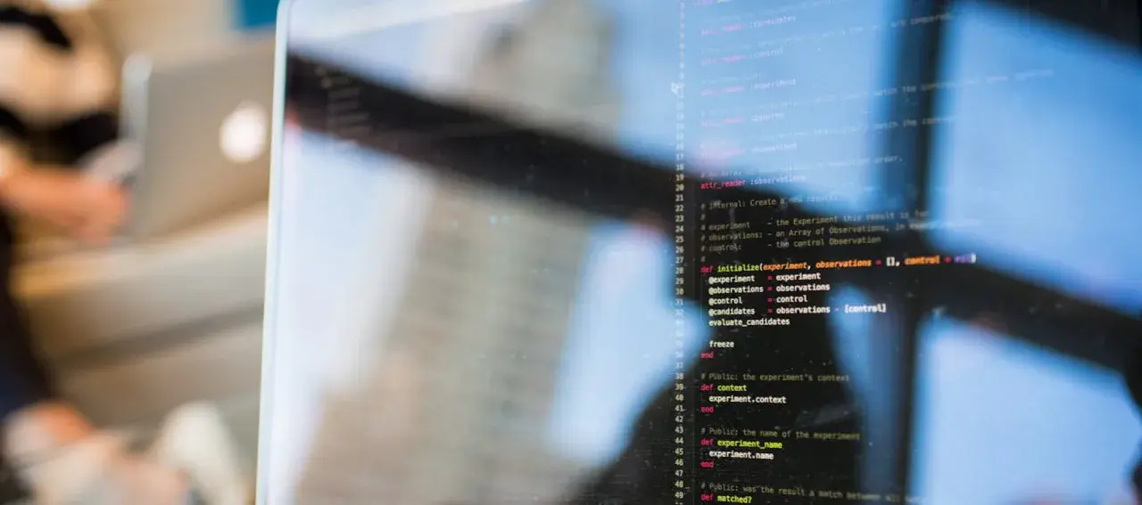 Kod w języku polskim, pisany na ekranie komputera, z odbiciem osoby pracującej w tle.