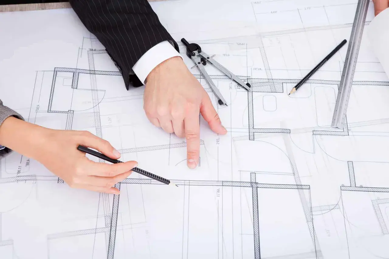 Rysunki techniczne domu, na których dwie osoby omawiają zmianę projektu po uzyskaniu pozwolenia na budowę.