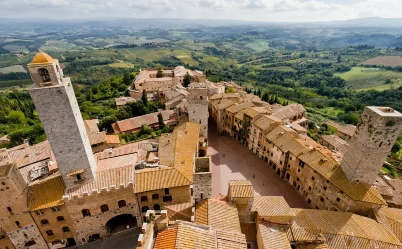 Panoramica aerea di San Gimignano, con le sue torri medievali che svettano tra i tetti di tegole rosse. Un paesaggio incantevole, tipico dei borghi vicino San Gimignano, immerso nel verde delle colline toscane.