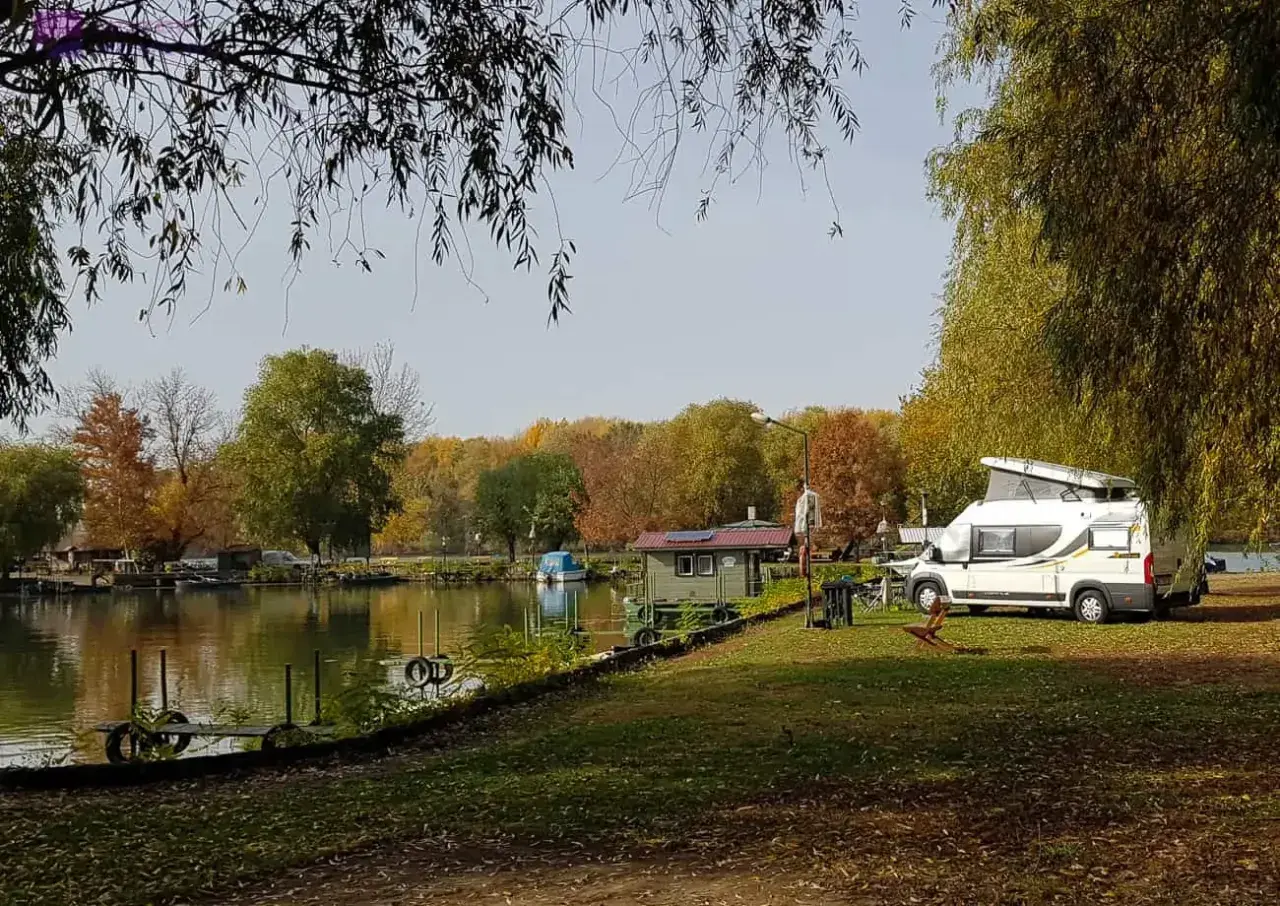 Jesień na Węgrzech. Kamper zaparkowany nad jeziorem, w tle kolorowe drzewa i mała chatka.