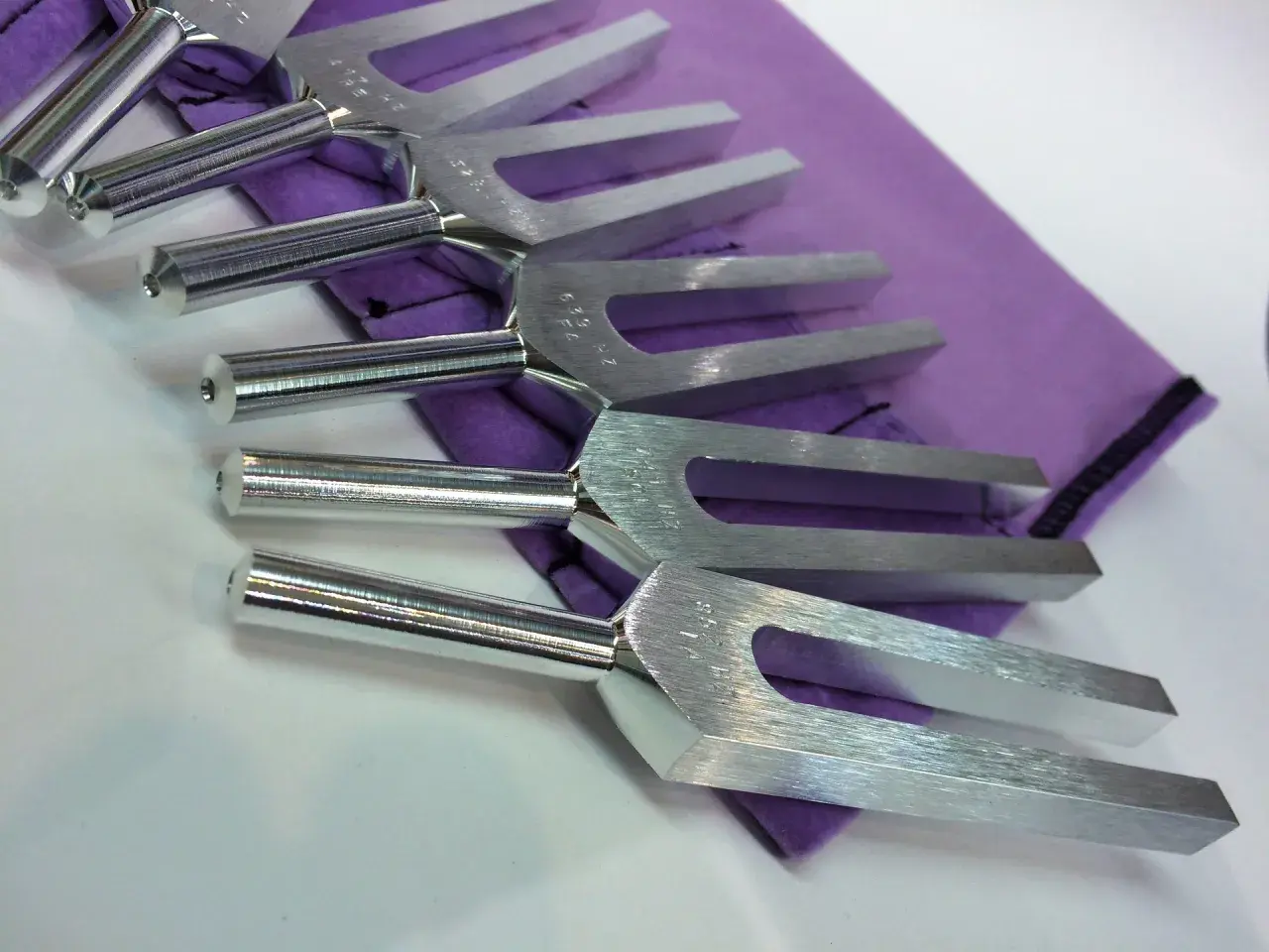 Un ensemble de diapasons en métal argenté repose sur un tissu violet. Ces outils de musique sont prêts à produire des sons purs.