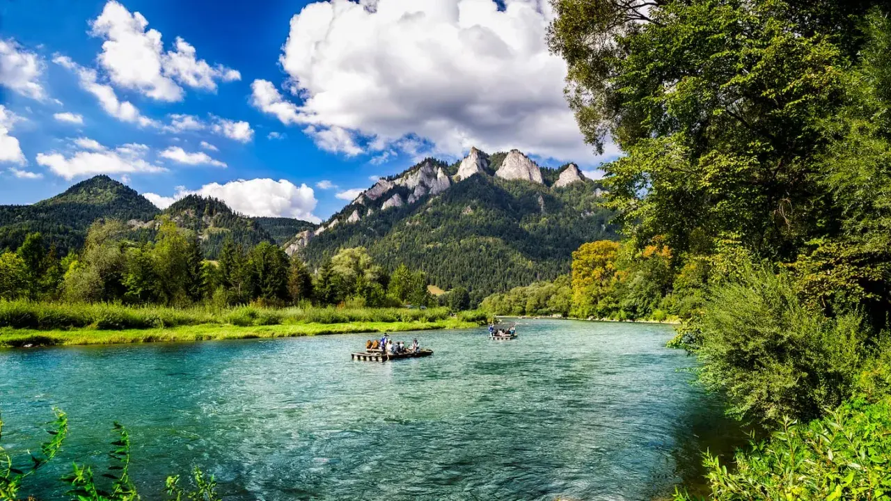 Flöße auf einem türkisfarbenen Fluss vor bewaldeten Bergen. Ein idyllisches Bild für Ausflugsziele Polen.