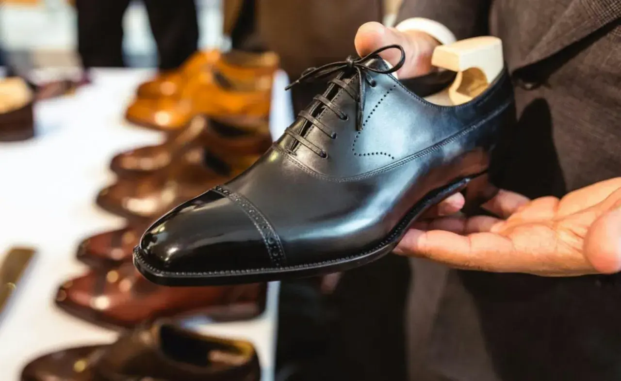 Main d'un homme tenant une chaussure noire brillante, prête à nourrir le cuir. D'autres chaussures en cuir sont alignées en arrière-plan.