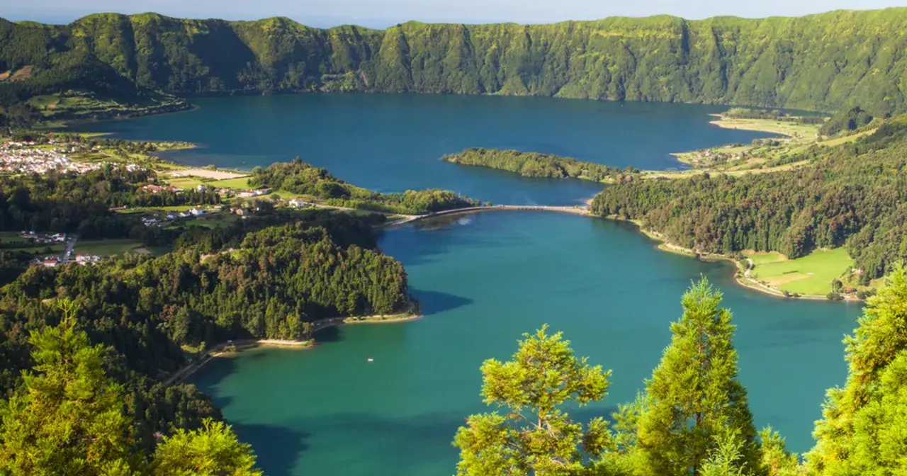 Malowniczy krajobraz portugalskiego archipelagu na Atlantyku: jezioro w kraterze wulkanicznym, otoczone zielonymi wzgórzami i niewielką wioską.