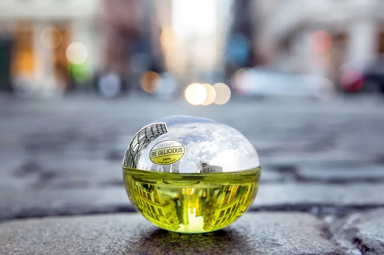 DKNY Be Delicious 100 ml, zielony flakon perfum w kształcie jabłka, odbijający miejski krajobraz.