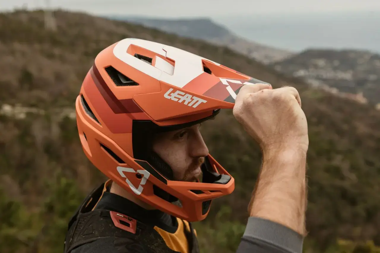 Uomo con casco integrale Leatt arancione, pronto per downhill. Il casco integrale significato è protezione totale.