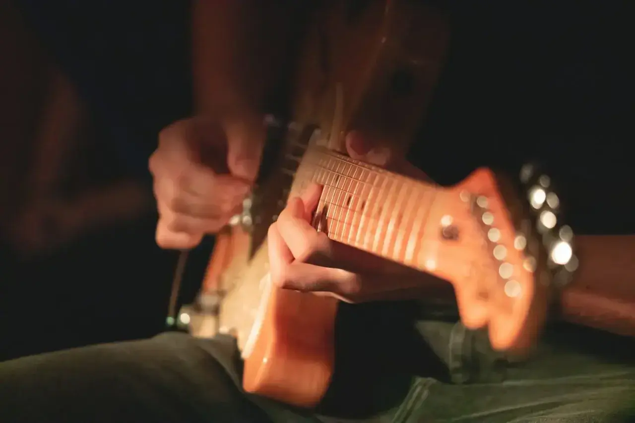 Intensywna nauka gry na gitarze elektrycznej. Dłonie ćwiczą akordy na gryfie, światło podkreśla drewno instrumentu.
