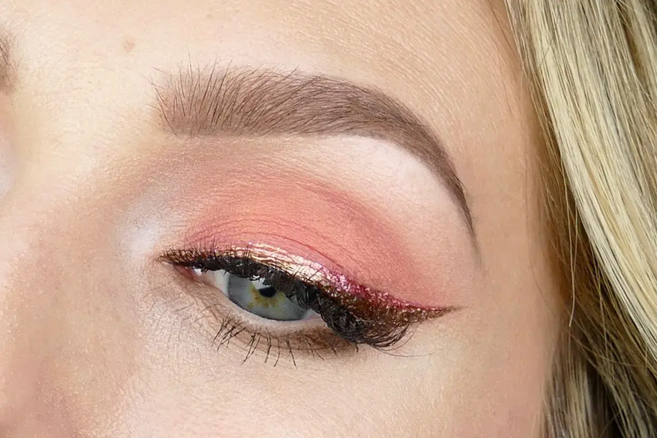 En närbild på ett öga med en vacker rosa sminkning. Ögonlocket har en mjuk rosa skugga och en glittrig eyeliner i guld och rosa.