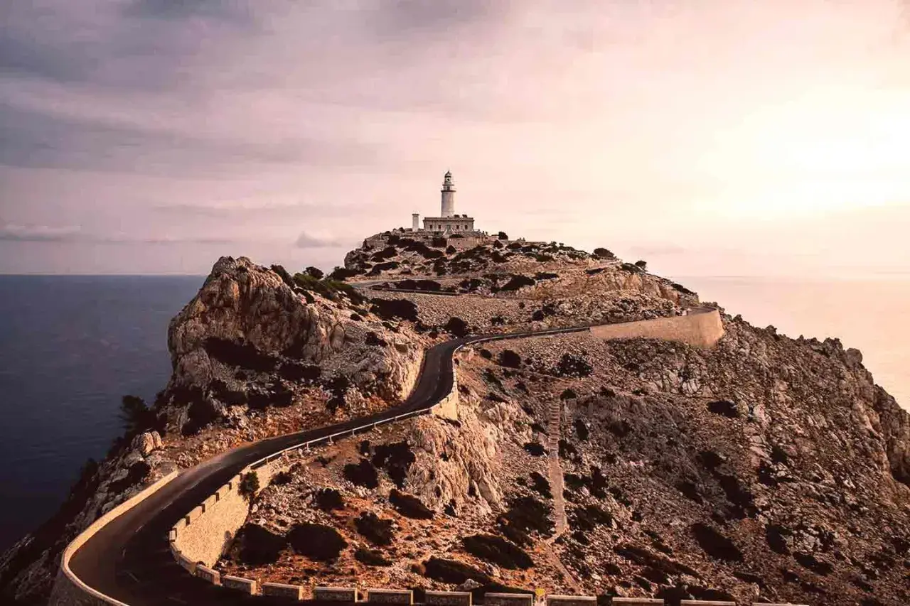 Faro en la cima de un acantilado rocoso, con una carretera serpenteante que asciende. Un paisaje de monumentos naturales impresionantes.