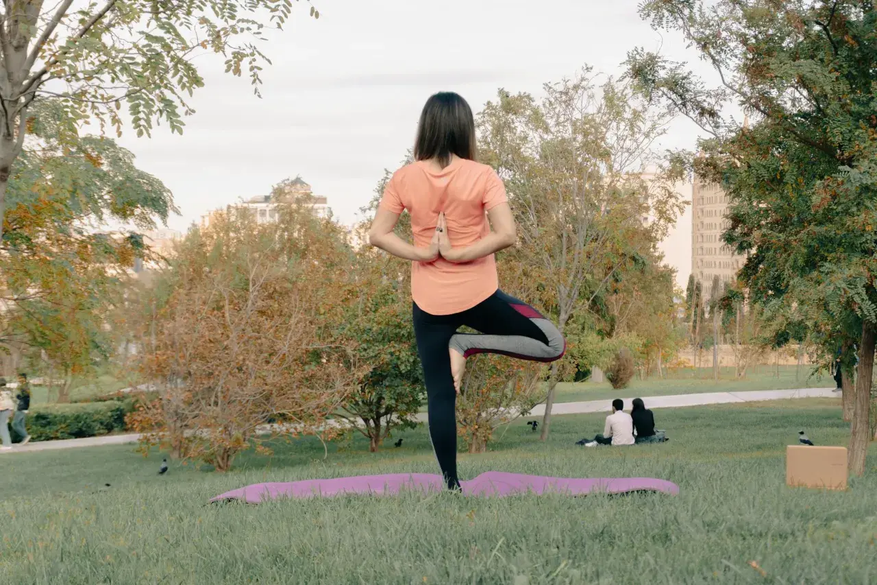 Mujer en postura de árbol, practicando yoga al aire libre en un parque.