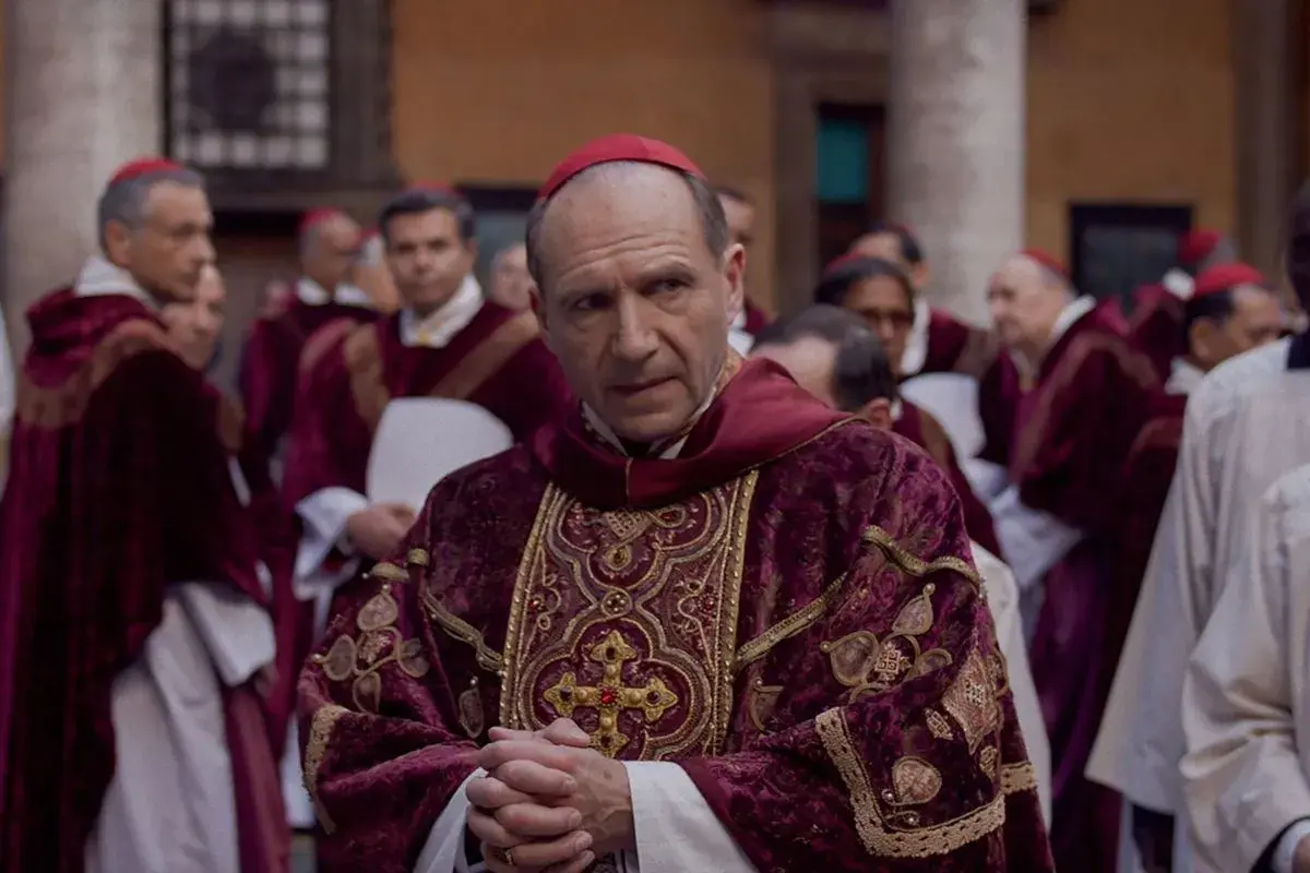 Scena z filmu o papieżu. Kardynał w bogato zdobionej szacie z czerwonym piuską. W tle inni duchowni.