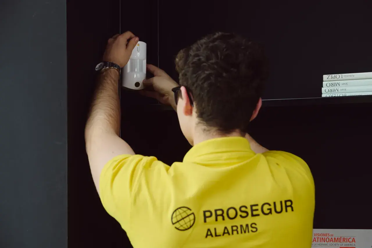 Técnico instala un sensor PIR blanco en una estantería, asegurando la protección del hogar.