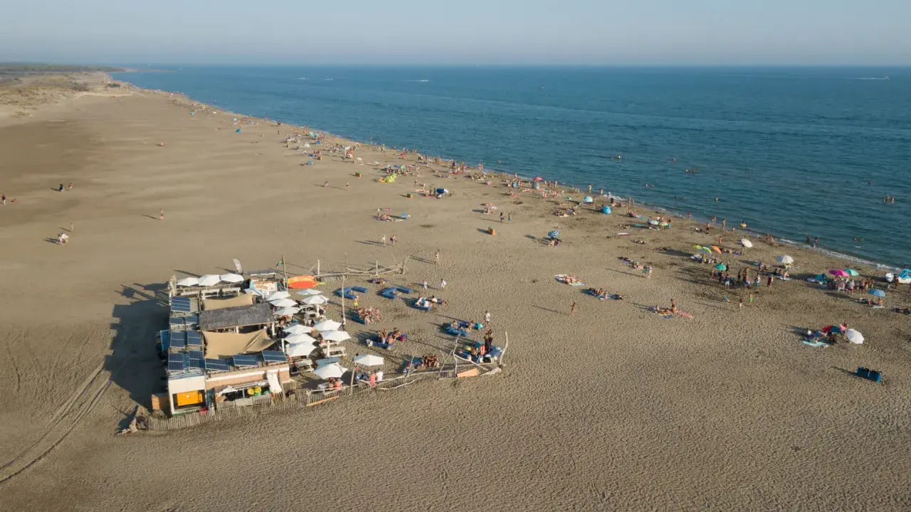 Vue aérienne d'une plage privée au Grau-du-Roi, avec des parasols, des transats et des baigneurs profitant du soleil et de la mer.