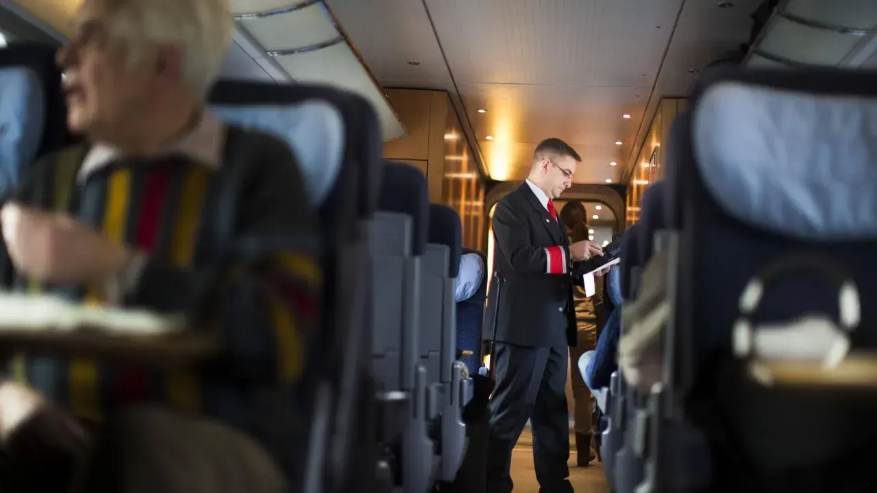 Ein Schaffner im deutschen Zugsystem prüft Tickets. Passagiere sitzen in den Reihen.