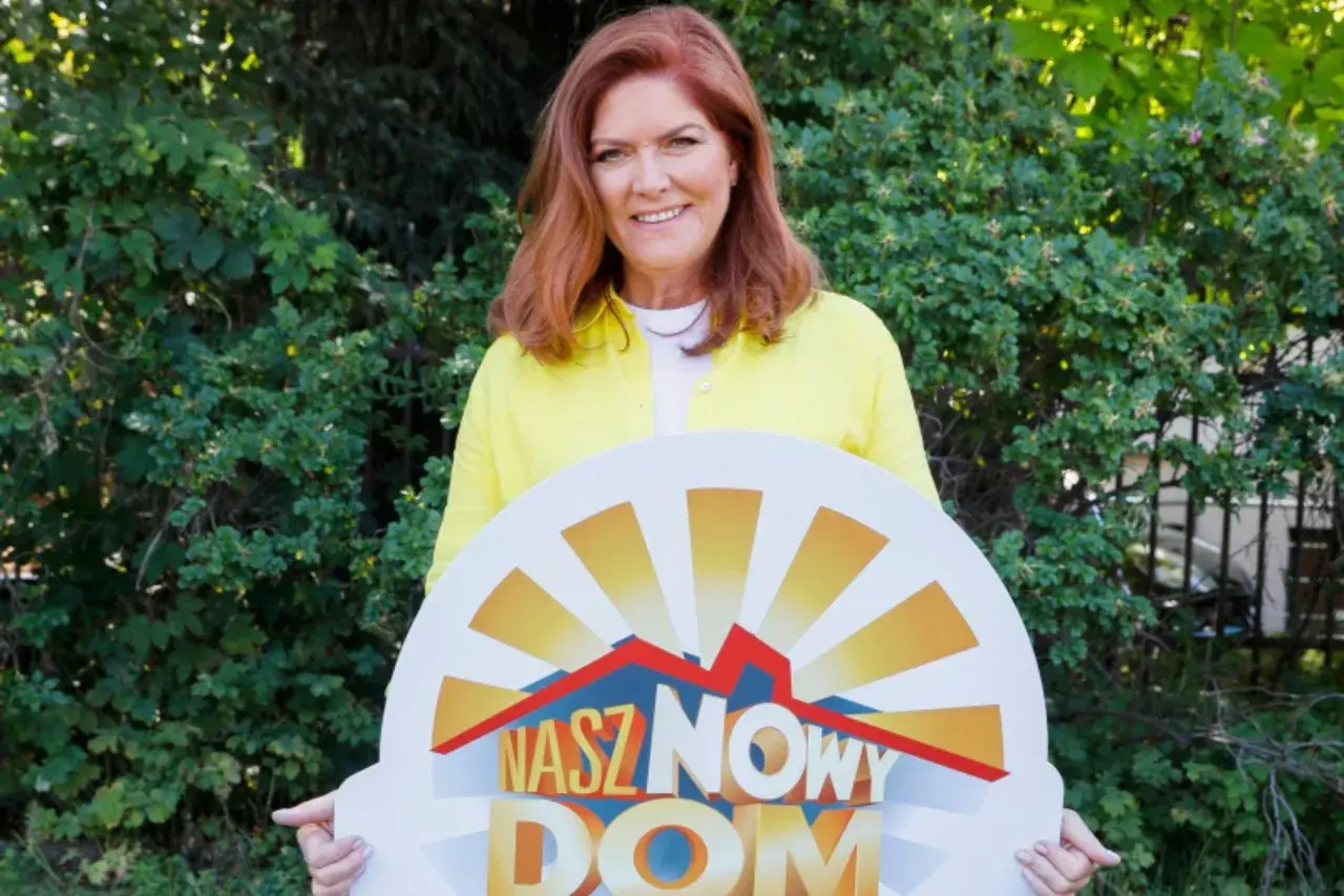 Katarzyna Dowbor z uśmiechem prezentuje tablicę z napisem "Nasz Nowy Dom".