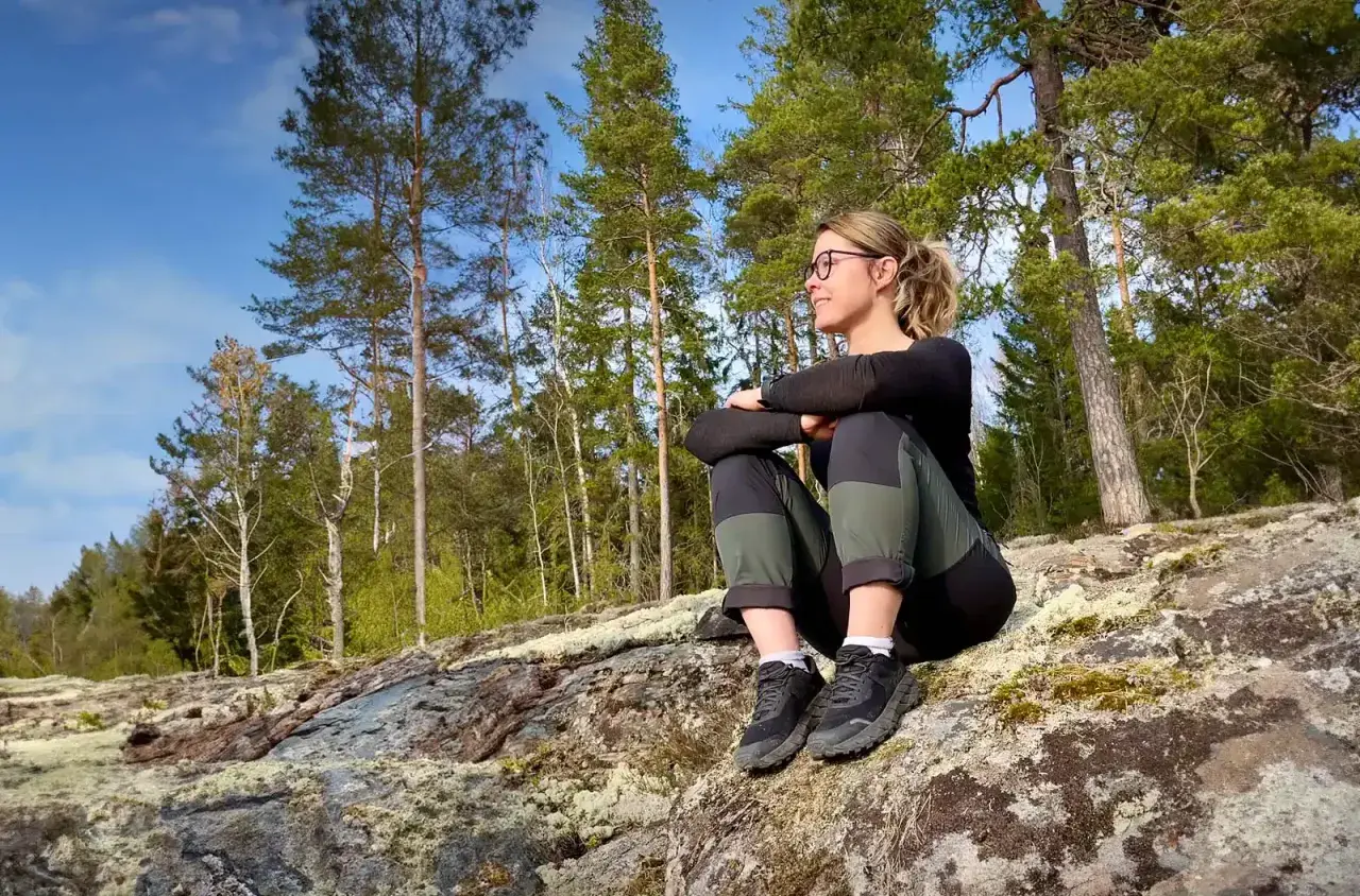 Kvinna vilar på en klippa bland tallar, njuter av utsikten. Perfekt för att utforska vandringsleder Stockholm.