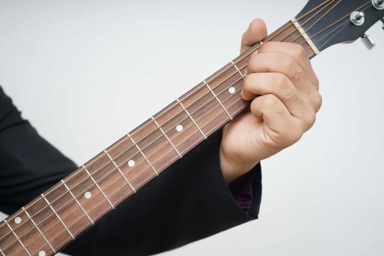 Dłoń dociska struny na gryfie gitary, rozpoczynając naukę gry na gitarze.