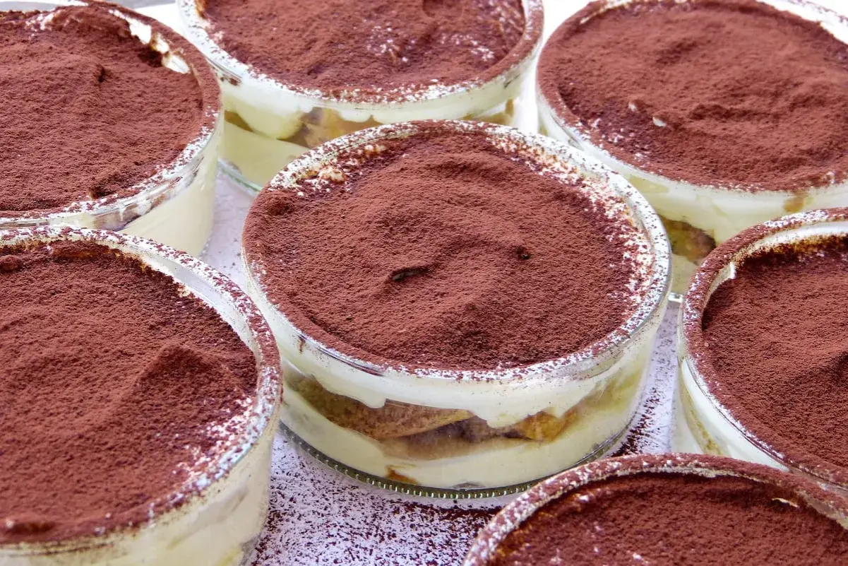 Varios vasitos de tiramisú, con capas de crema y bizcocho, espolvoreados con cacao. Los tiramisú ingredientes se ven deliciosos.