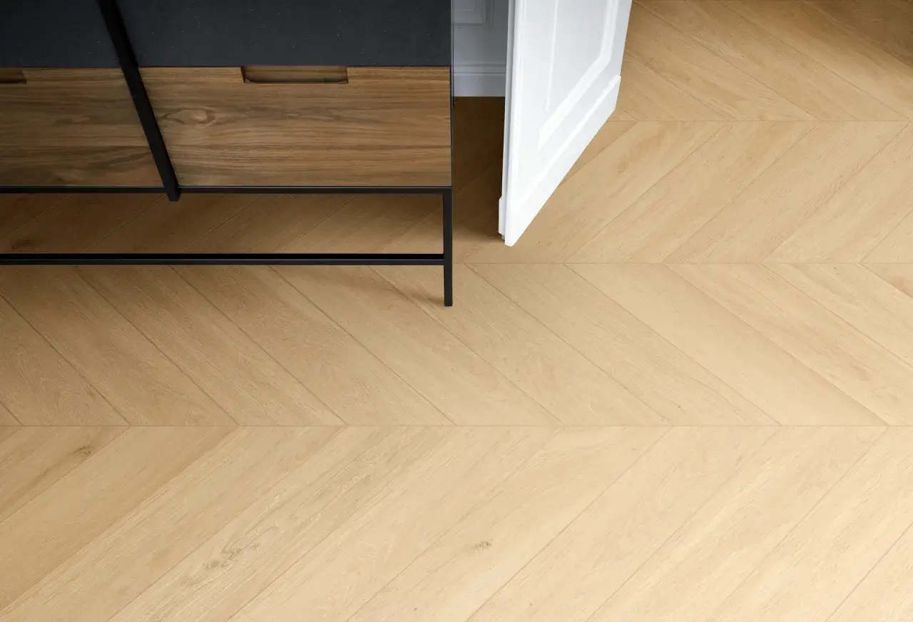 Posa di un elegante parquet in gres porcellanato effetto legno, con un motivo a spina di pesce che si estende verso una porta bianca aperta.