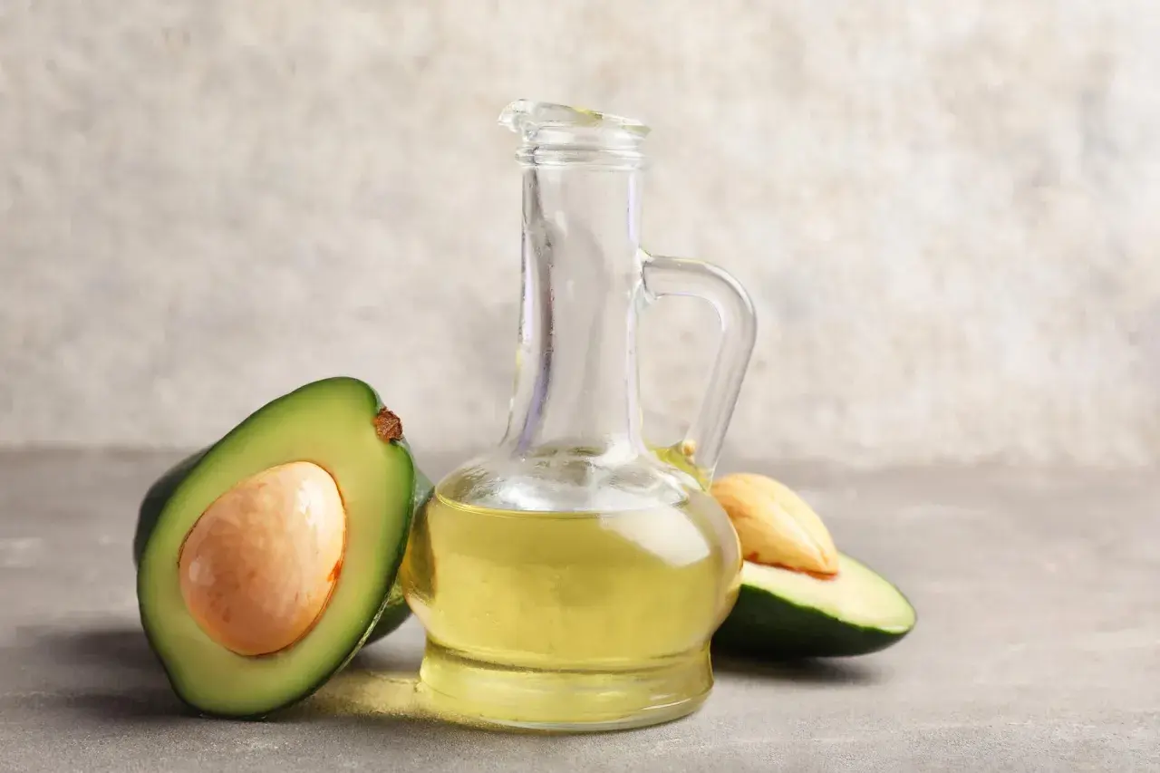 Bouteille en verre remplie d'huile avocat dorée, avec des moitiés d'avocat frais autour.