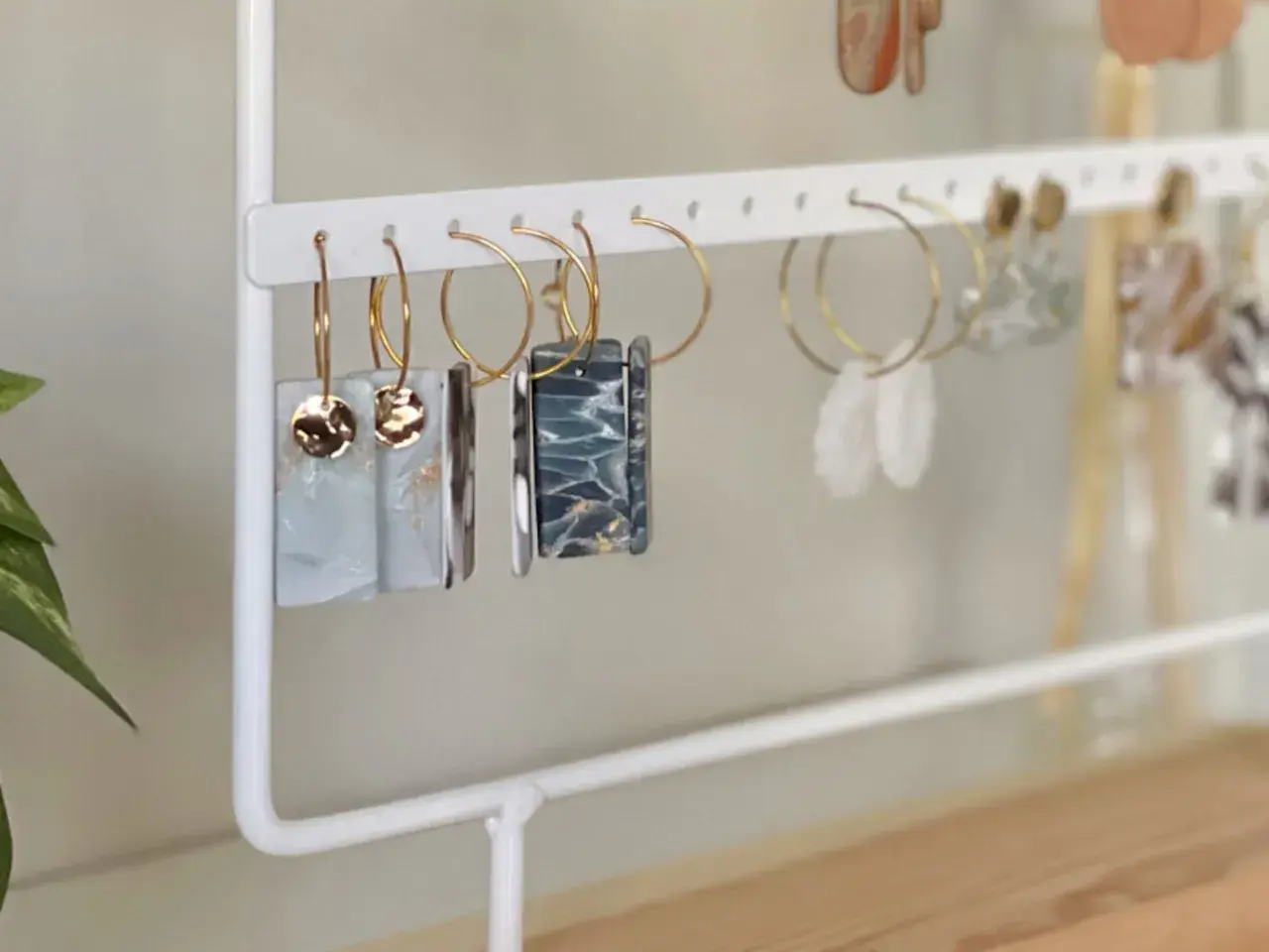 Un porta pendientes blanco exhibe varios pares de aretes colgantes, algunos con detalles dorados y otros con diseños marmoleados.