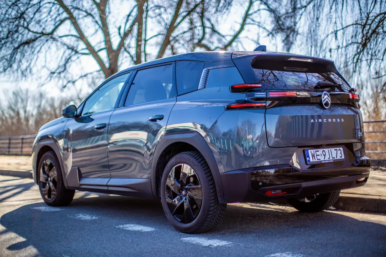 Ciemnoszary Citroën C5 Aircross Hybrid zaparkowany pod drzewami. Widok z tyłu, z tablicą rejestracyjną WE 9JL73.