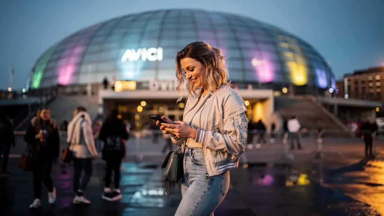 Glad kvinna med mobil framför Avicii Arena, Stockholm. Kanske väntar på en kyrkokonsert i Stockholm?