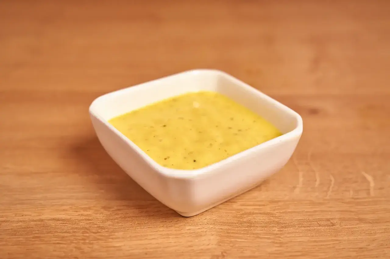 Un cuenco blanco contiene una cremosa salsa miel y mostaza, lista para acompañar tus platos.