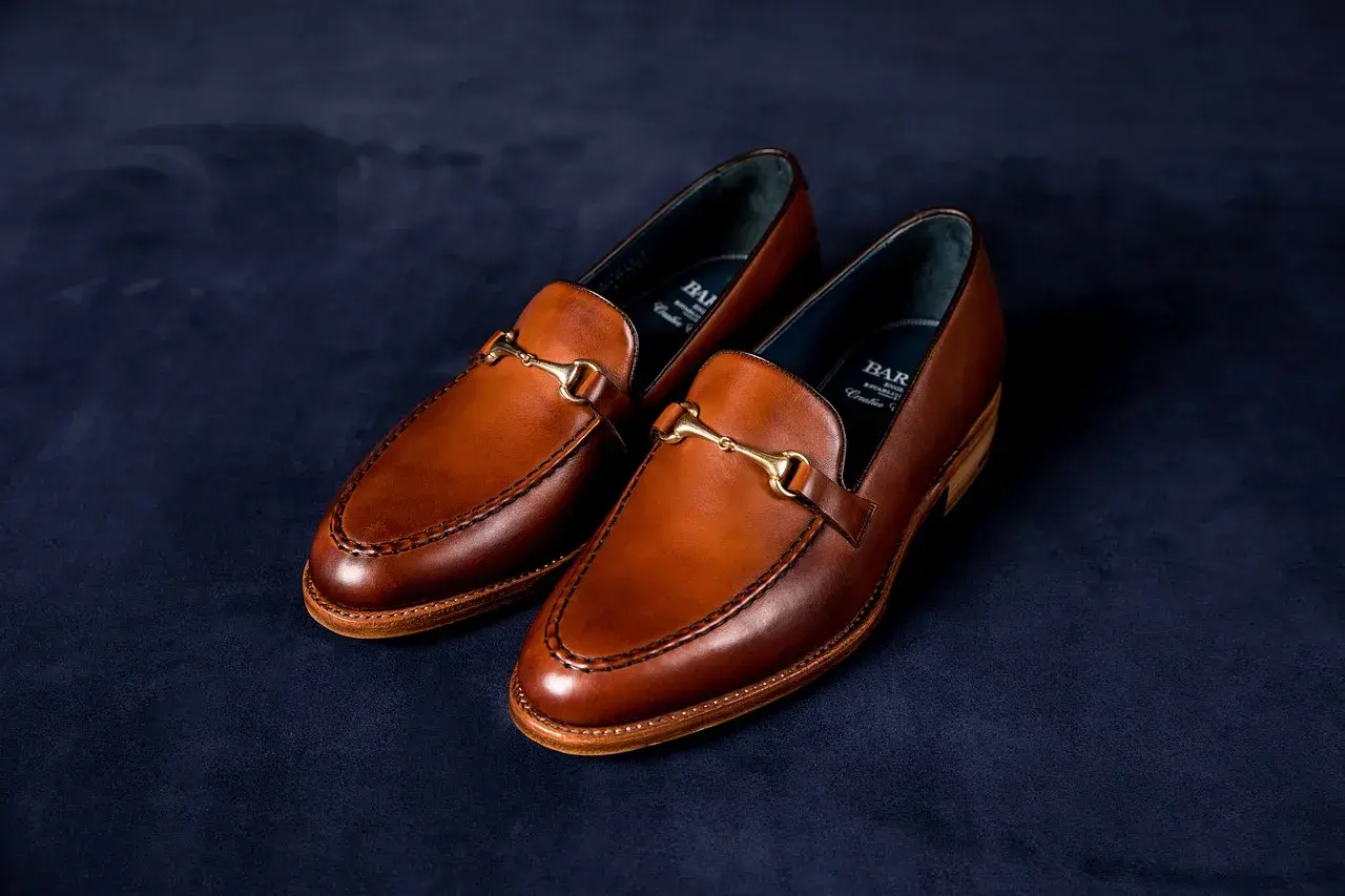 Eleganckie, brązowe loafersy do sukienki z ozdobnym złotym elementem, idealne na specjalne okazje.