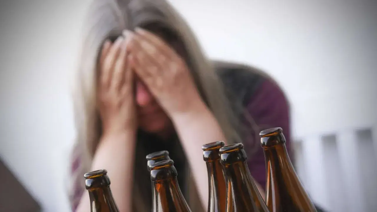 Verzweifelte Frau mit Händen vor dem Gesicht, umgeben von Bierflaschen. Ein Symbol für die Gefahren von Alkohol und die mögliche Entwicklung von Alkohol-Demenz.