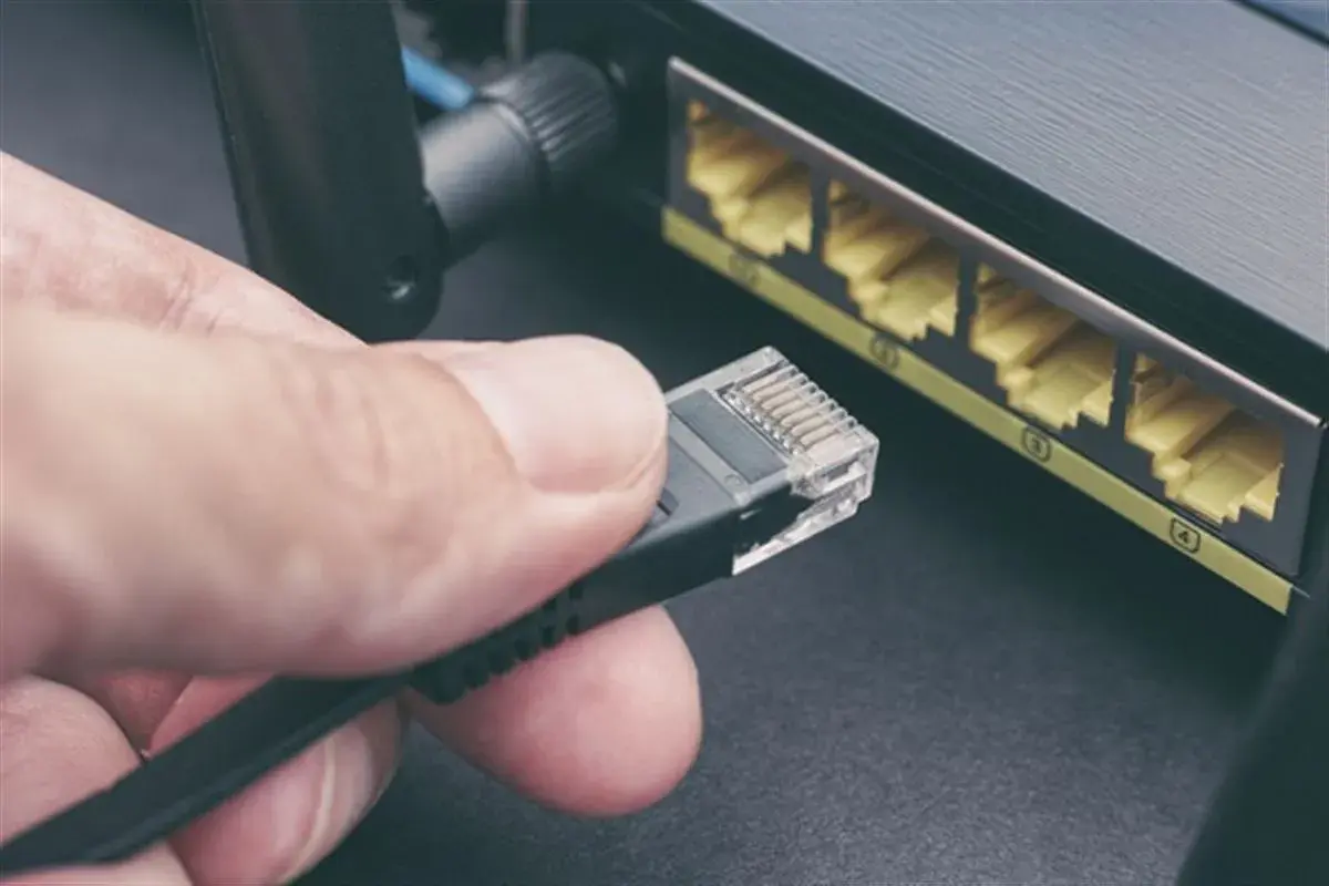Main d'une personne tenant un câble rj45, prêt à le brancher dans un routeur. Connexion réseau.