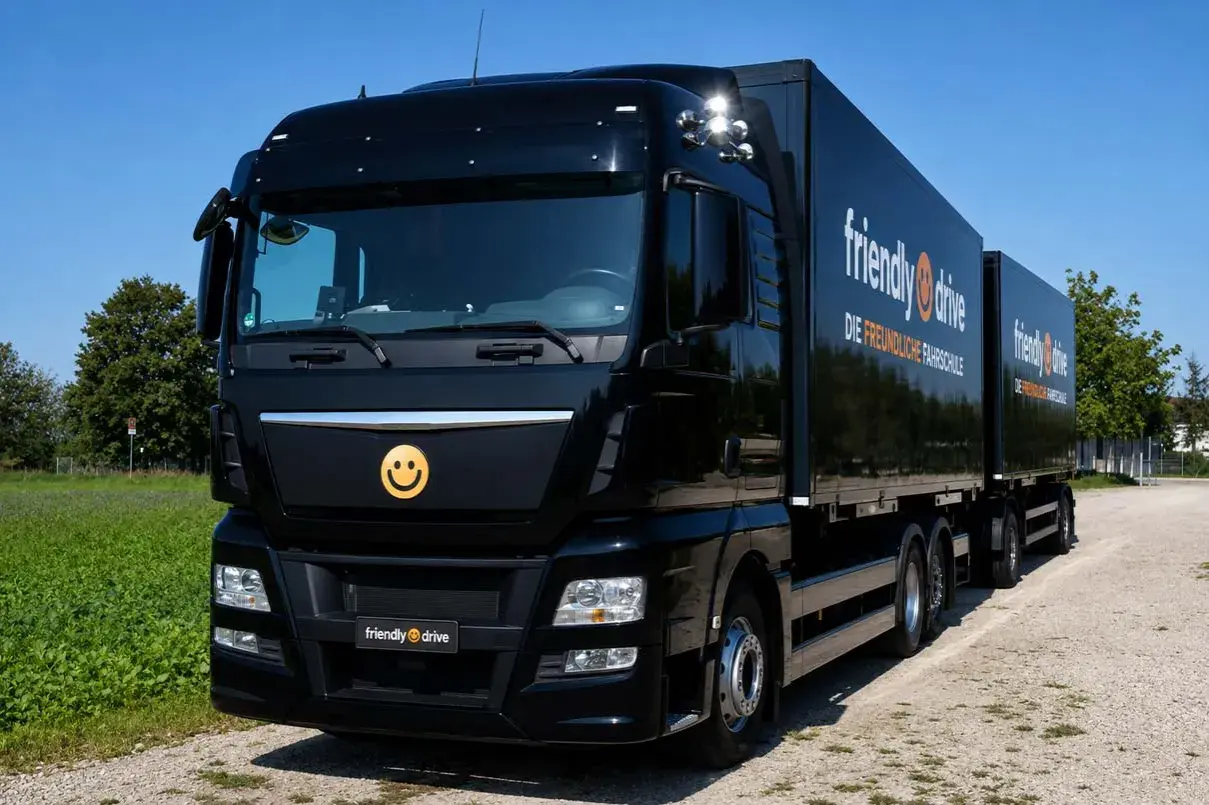 Schwarzer Lkw mit Anhänger, Werbung für "friendly drive - Die freundliche Fahrschule". Ein Smiley-Logo ziert die Front.