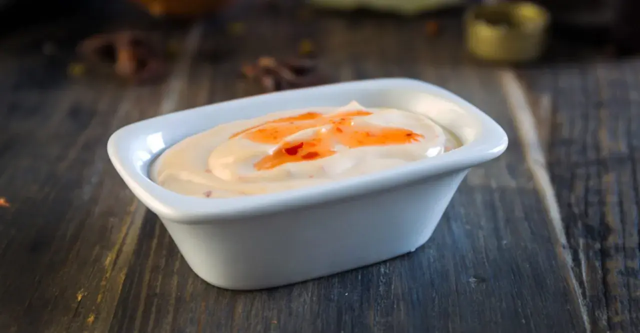 Krämig sås med en virvel av söt chili sås, serverad i en vit skål på en träyta.