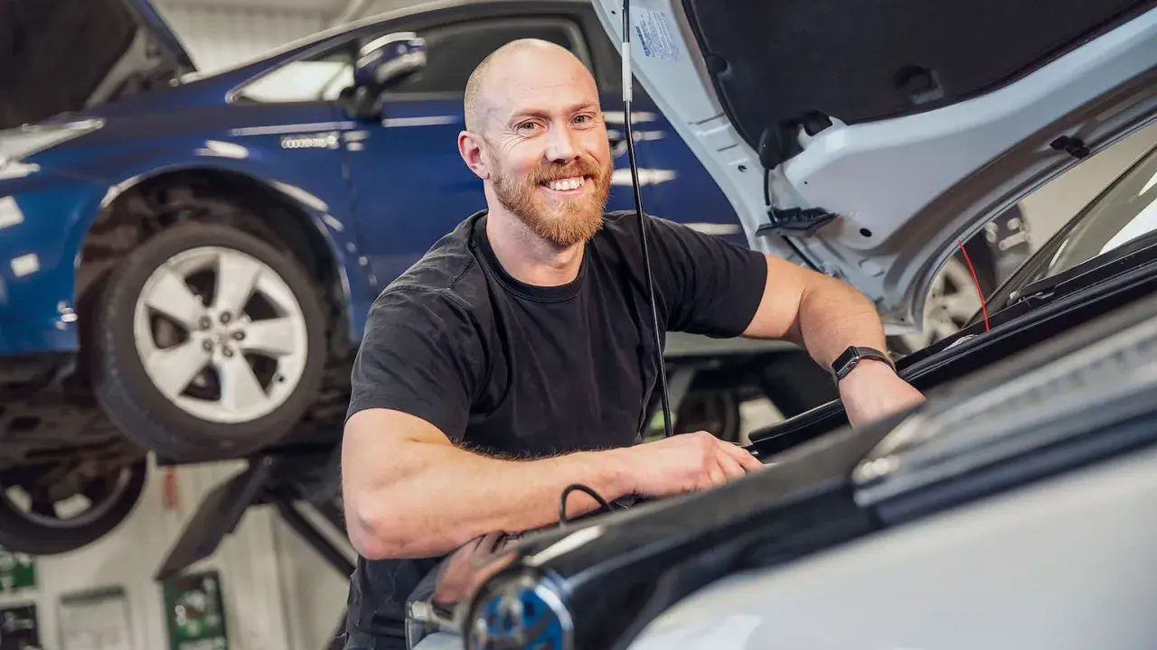 Glad mekaniker arbetar med en b1 service på en Mercedes. En blå bil syns i bakgrunden.