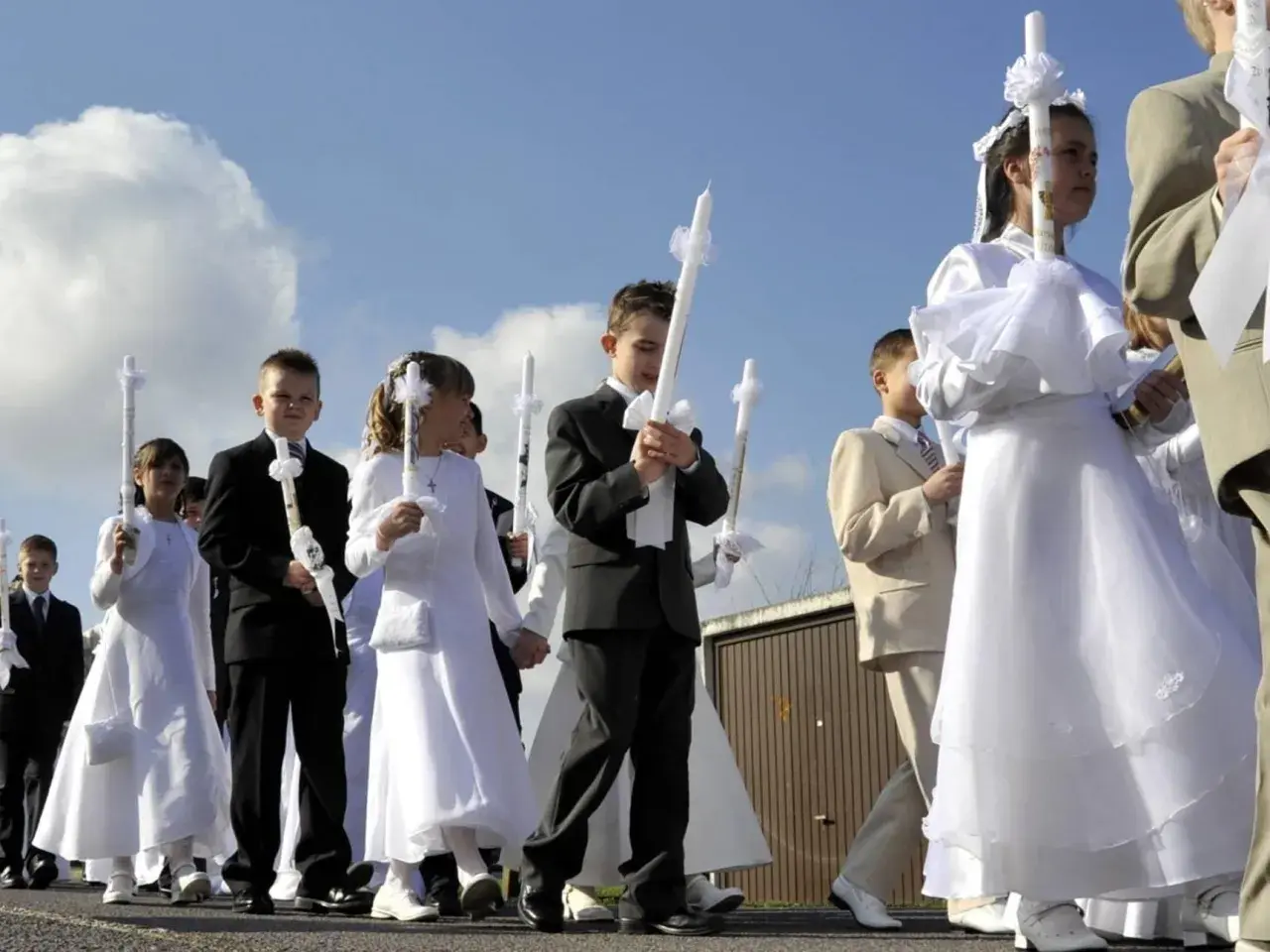 Kinder in festlicher Kleidung, oft weiße Kleider und Anzüge, tragen Kerzen zur Kommunion. Als Gast zur Kommunion zieht man sich festlich, aber dezent an.