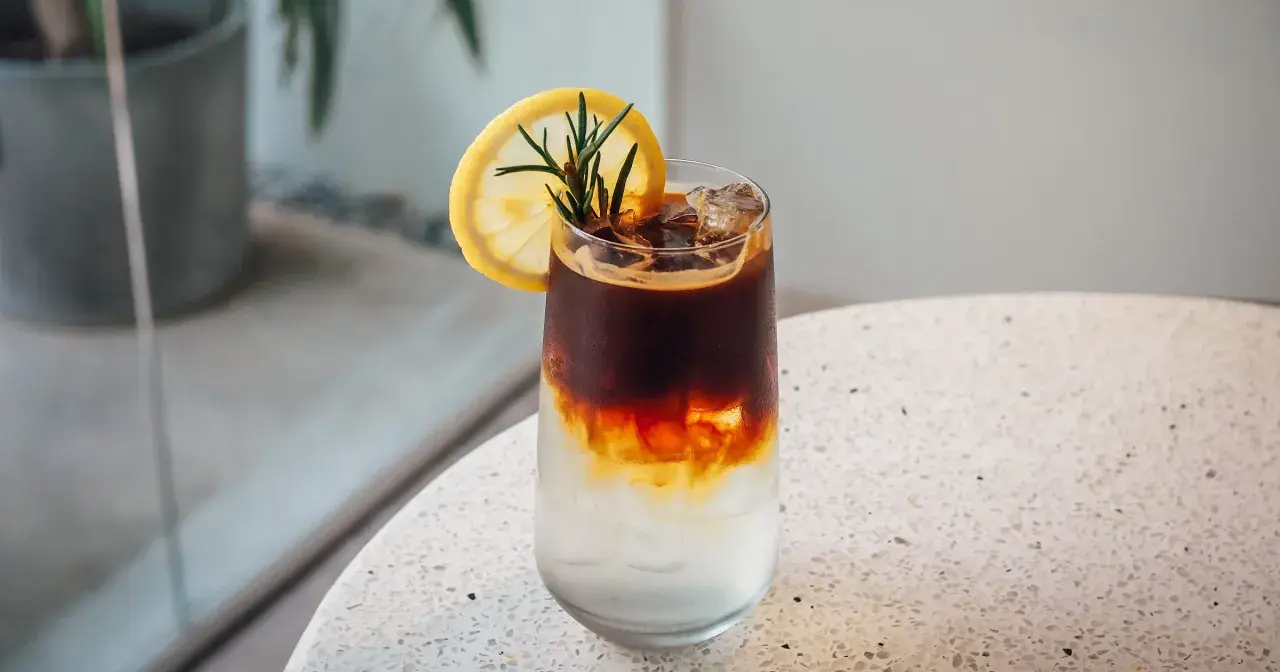 Orzeźwiający tonic espresso z plasterkiem cytryny i rozmarynem, idealny na upalny dzień.