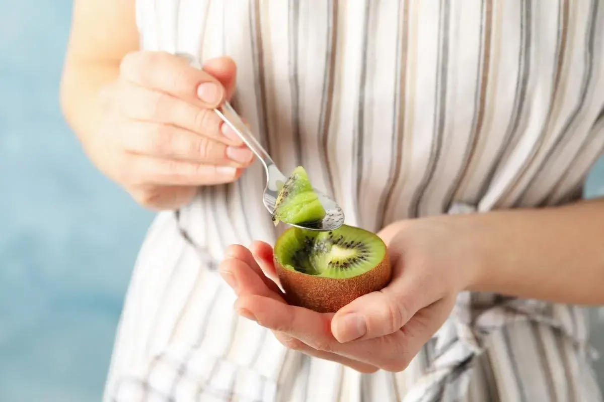 Kobieta trzyma w dłoniach połówkę kiwi i łyżeczkę z kawałkiem owocu.