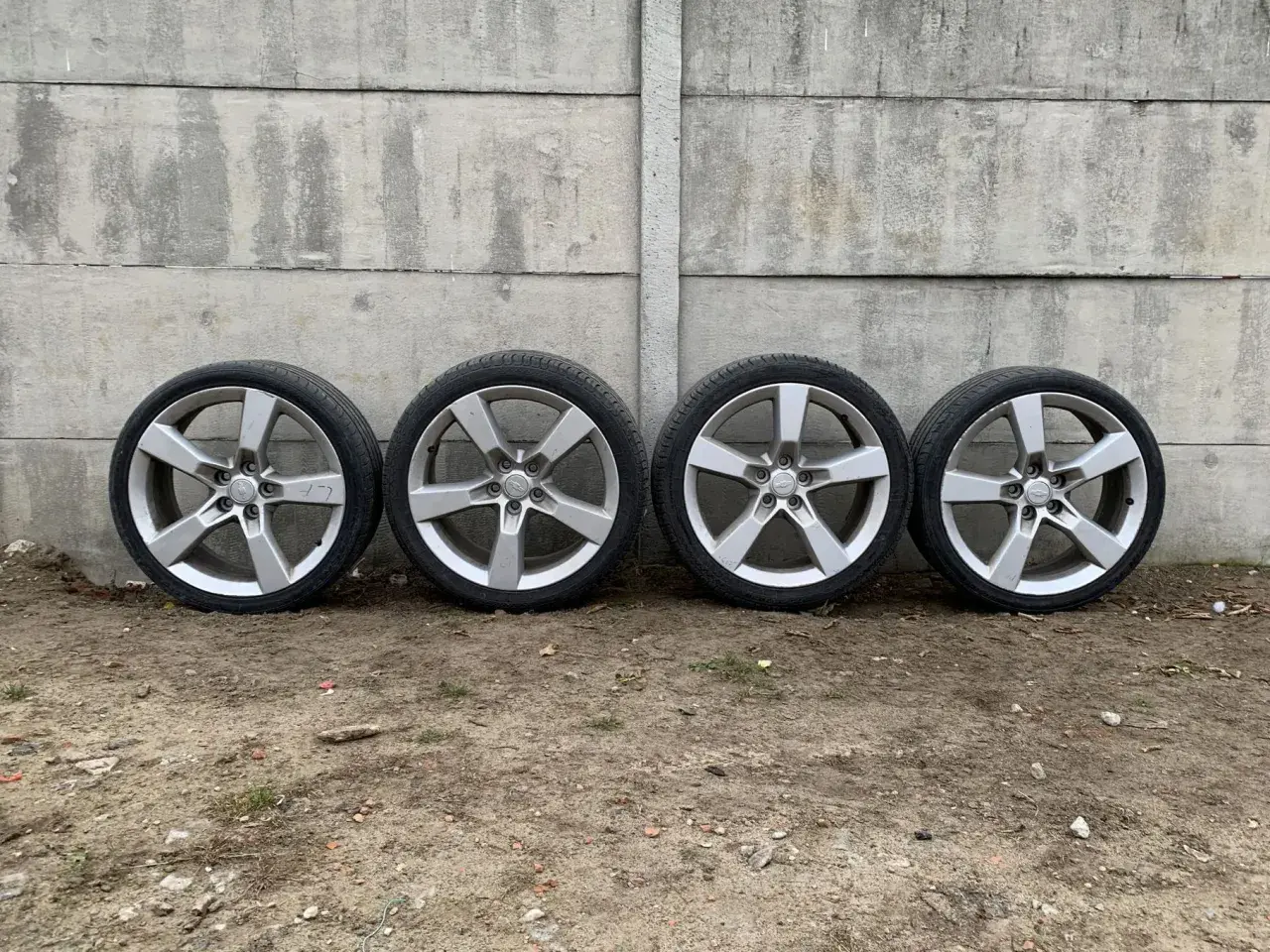 Cztery aluminiowe felgi z oponami Camaro SS na tle betonowego muru.