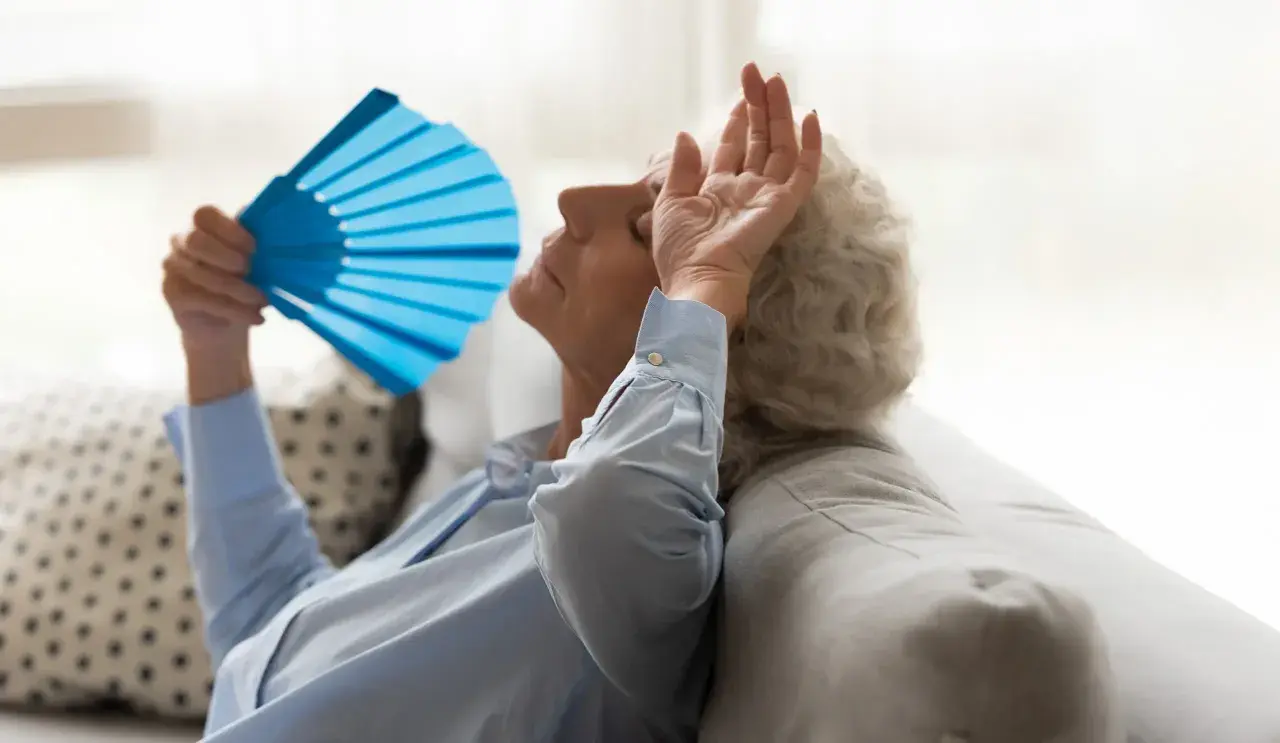 Une femme âgée s'évente avec un éventail bleu, montrant les effets de la chaleur sur les personnes âgées.