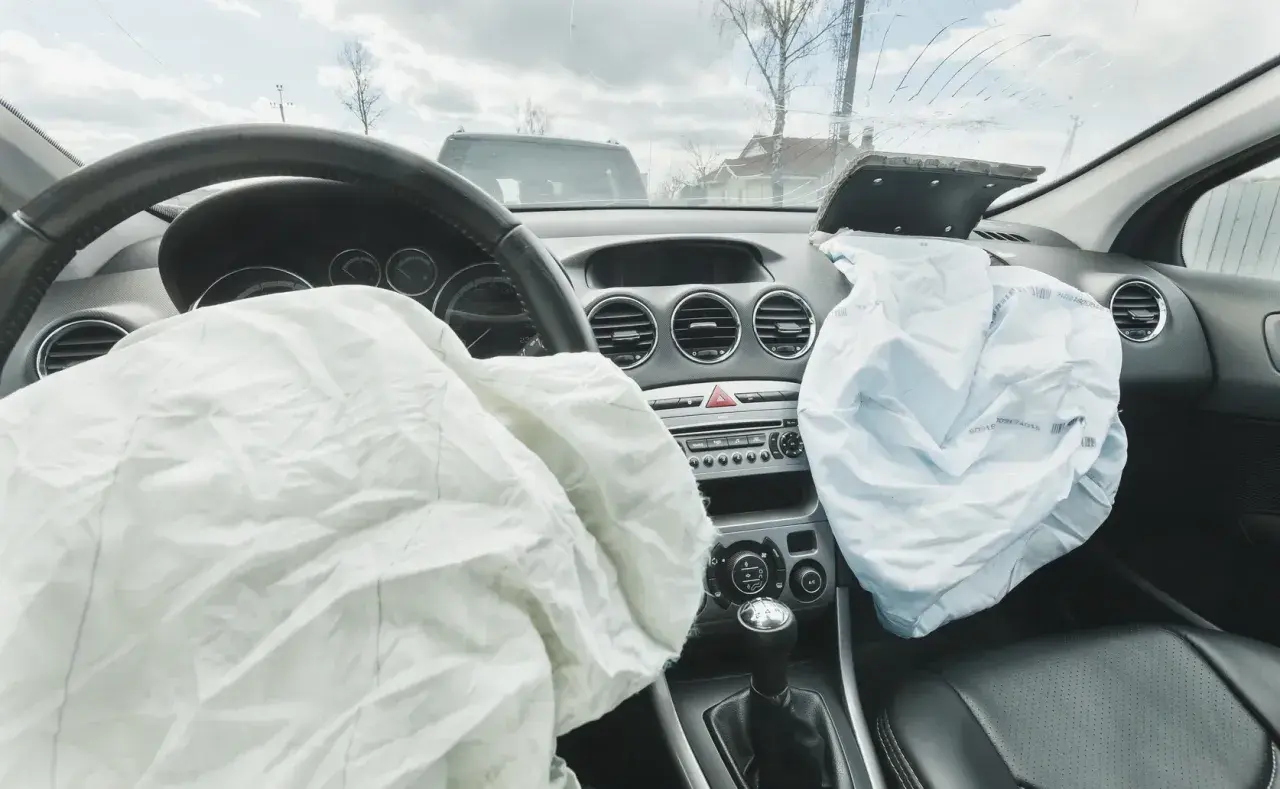 Wnętrze samochodu po wypadku. Rozwinięty **airbag** kierowcy i pasażera, pęknięta przednia szyba.