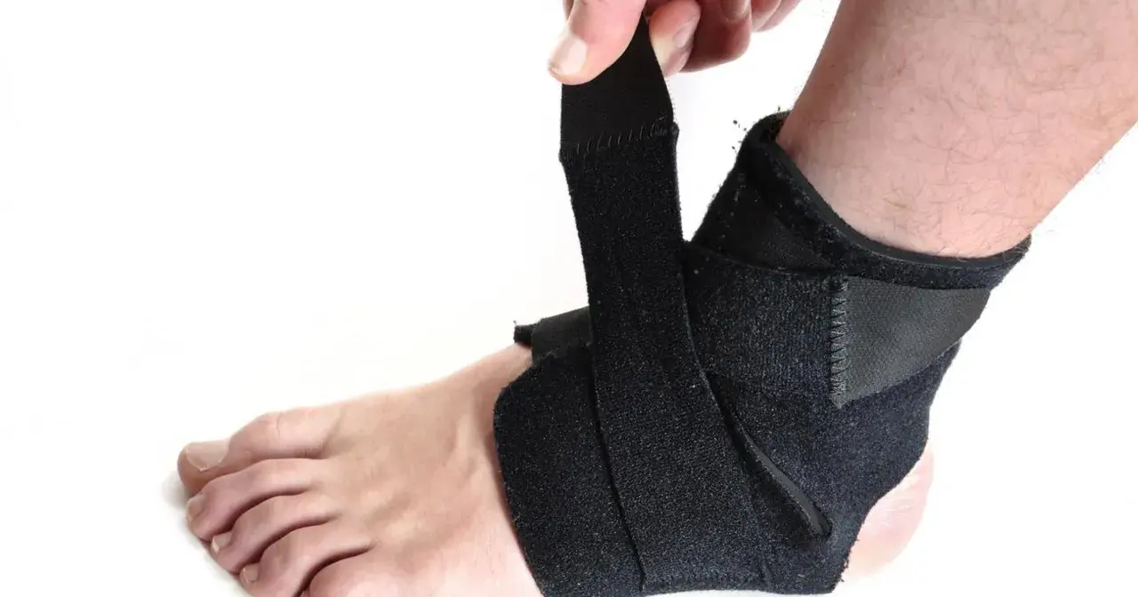 Dłoń zapina czarny stabilizator na kostce. Zapewnia wsparcie i ochronę podczas aktywności.