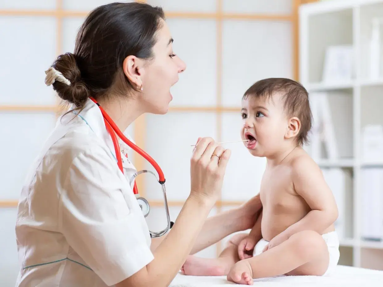 Medico esamina la gola di un bambino con abbassalingua, controllando sintomi di laringite bambini.