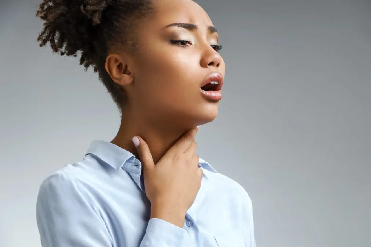Femme portant la main à sa gorge, bouche ouverte, possiblement atteinte de scarlatine adulte.